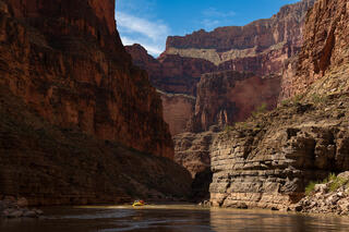 A small yellow raft beneath dark cliffs with a touch of blue sky and clouds.