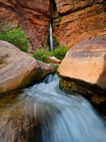 A very tall waterfall becomes a stream winding its way through boulders in the Grand Canyon.