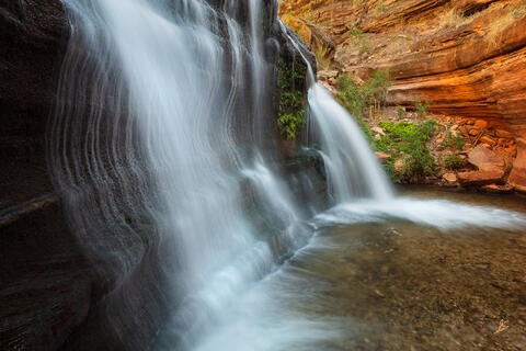 Waterfalls in a dark narrow gorge with red sandstone in the background. Grand Canyon National Park.