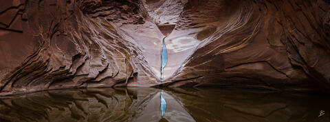 In North Canyon, a small sliver of water drips into a pool of water reflecting the surrounding cliffs in the Grand Canyon.