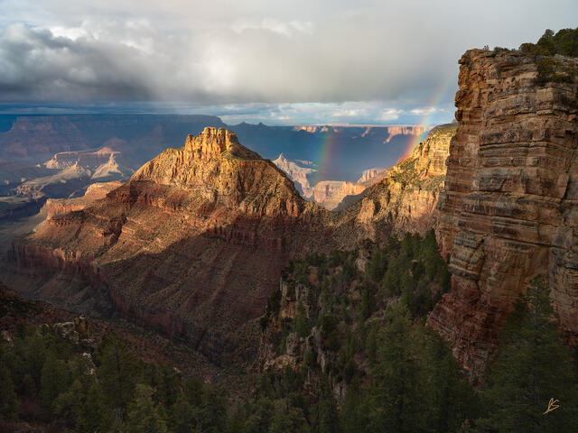 Rainbows in the Grand Canyon with golden cliffs and clouds in the sky.