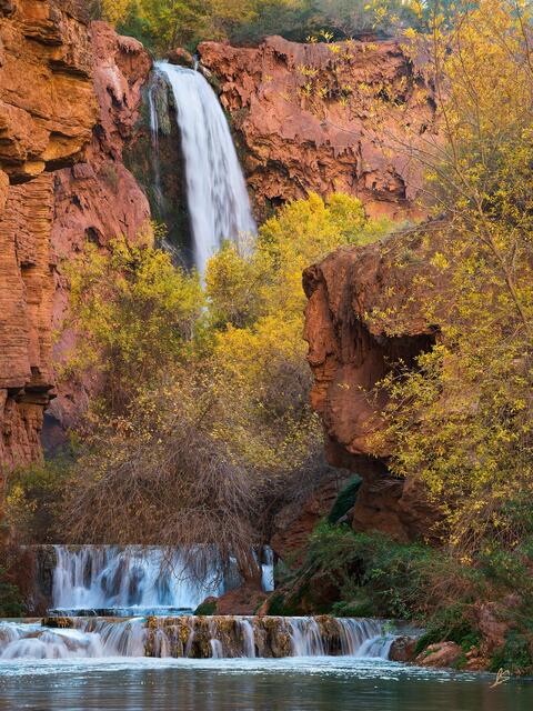 Orange and red cliffs and trees with yellow leaves surround a beautiful waterfall.