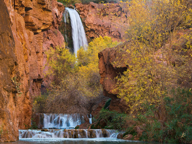 Orange cliffs and trees with yellow leaves surround a beautiful waterfall.