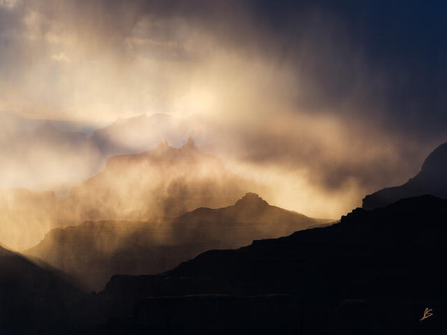 Rain falling into the Grand Canyon is backlit by the setting sun, causing it to take on golden hues.
