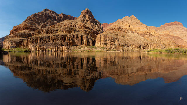 Tall cliffs in sunlight reflecting in the Colorado River deep in the Grand Canyon.