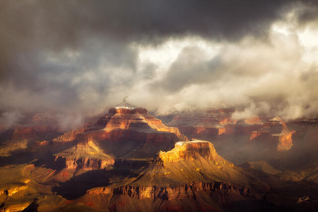 Low-hanging ragged clouds over red rock cliffs dusted with snow.