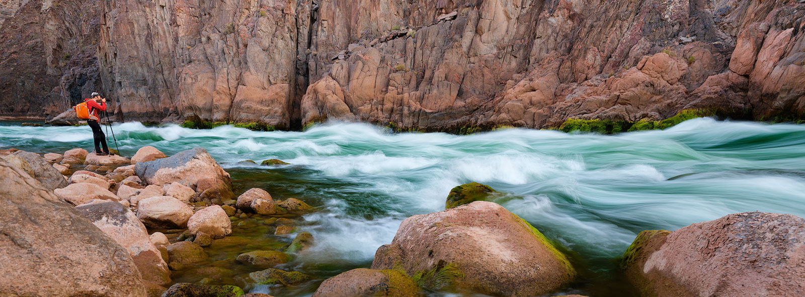 A photographer stands alongside Granite Rapid on the Colorado River in the Grand Canyon.