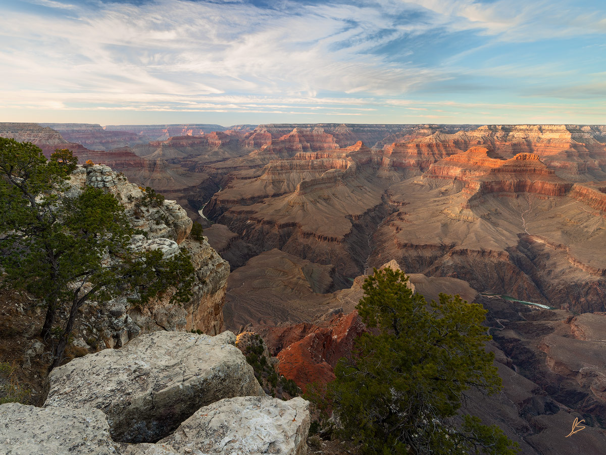The red and orange cliffs of the Grand Canyon with clouds in a blue sky.