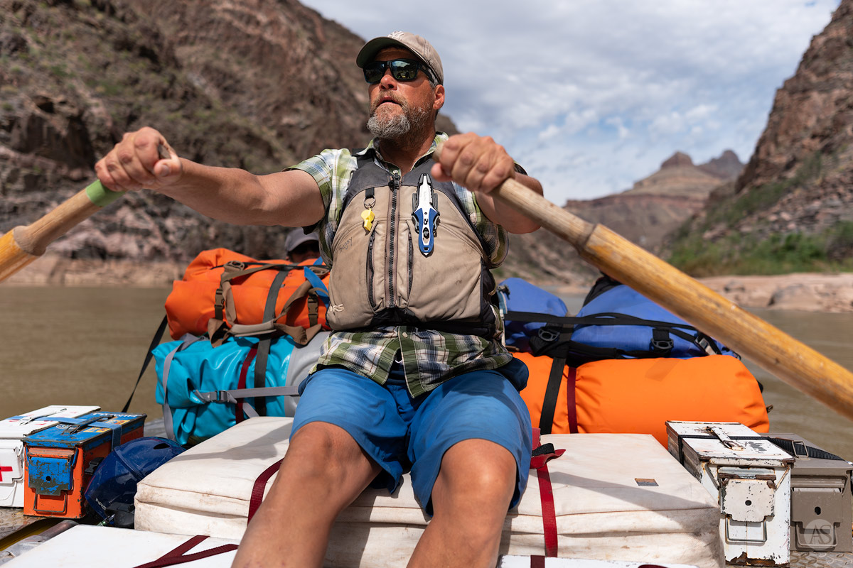 A river guide with his hands on the oars stares downstream, studying the current of the Colorado River in the Grand Canyon.