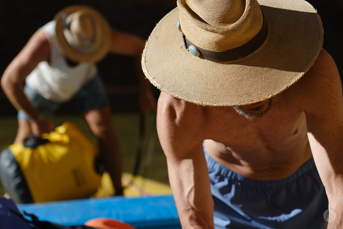 Two men wearing sun hats work on a raft on the Colorado River in the Grand Canyon.
