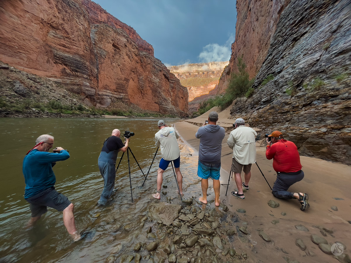 Several photographers with cameras on tripods photographing the Colorado River and the Grand Canyon with stormy light.
