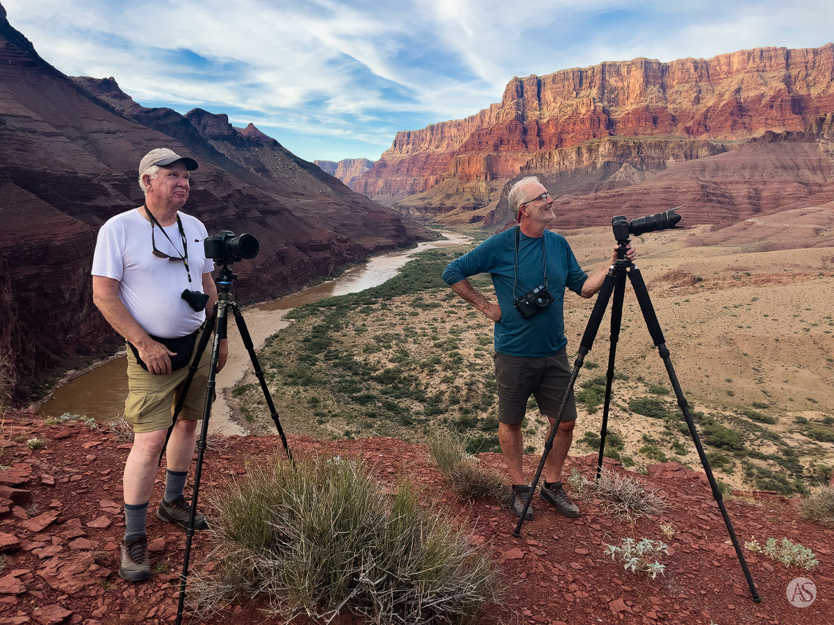 Two photographers with cameras on tripods photograph the Grand Canyon with the Colorado River in the background.