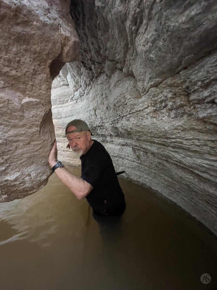 A photographer stands in a pool of water in a slot canyon while searching for new compositions.