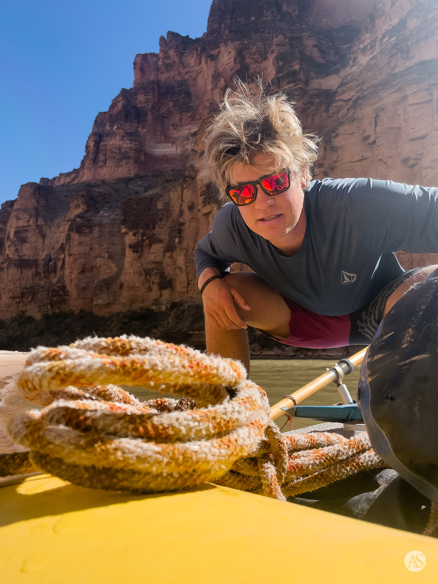 A Grand Canyon river guide with sunglasses on poses for the camera as he stands on his yellow raft.